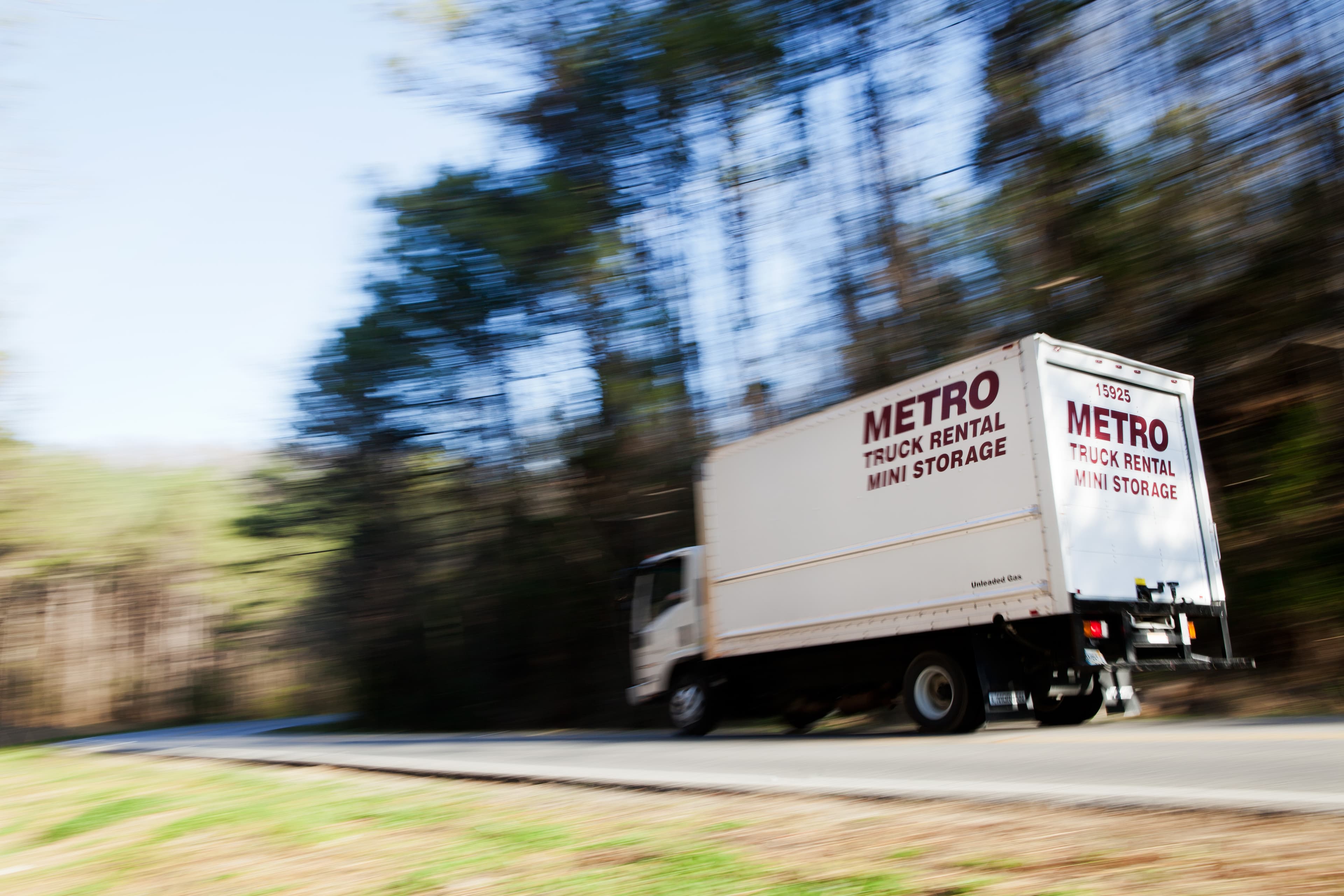 Metro truck driving quickly down a tree-lined road.